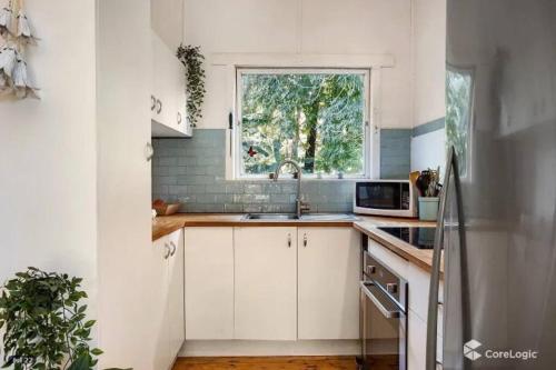 eine weiße Küche mit Spüle und Fenster in der Unterkunft Seabreeze Cottage Bundeena in Bundeena