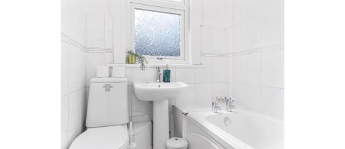 a white bathroom with a sink toilet and a window at City Escape: Sleek and Comfy 3 BR House w/ Garden in Hither Green