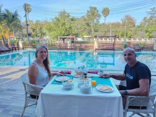 a man and woman sitting at a table in front of a pool at Senesothxuene Hotel in Muang Không