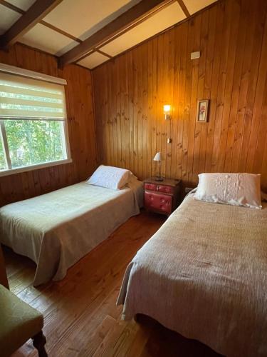2 Betten in einem Zimmer mit Holzwänden und einem Fenster in der Unterkunft Cabañas Vista al Lago in La Ensenada