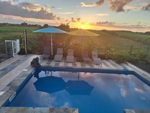 a pool with chairs and an umbrella and the sunset at L'EDEN DE JOSEPHINE in Le Moule