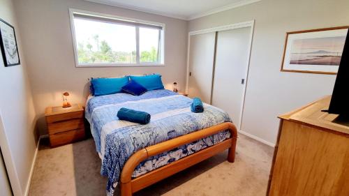 a bedroom with a bed with blue pillows and a window at Clarks Beach Getaway in Clarks Beach