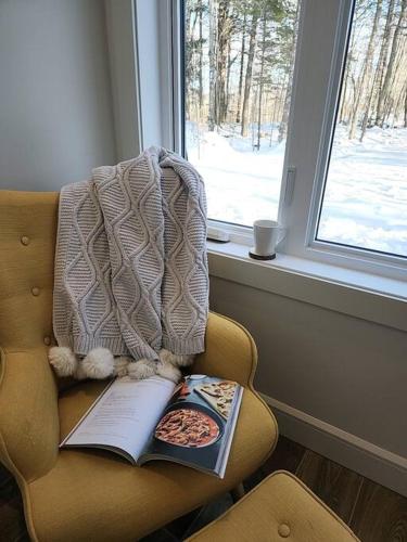 a blanket and a book on a chair with a window at Chalet TERRE en harmonie avec la nature, Tremblant in Lac-Superieur