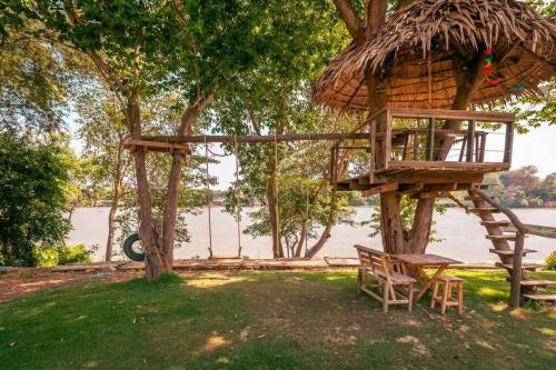 a tree house with a bench and a chair at Kaitoon's River House in Ratchaburi