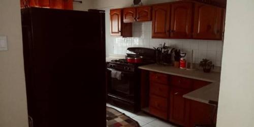a kitchen with wooden cabinets and a black refrigerator at Portmore Havens 1Bedroom EntireGuest House in Portmore