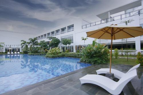 a swimming pool with an umbrella and a white chair at Raja Hotel Kuta Mandalika Resort & Convention in Kuta Lombok