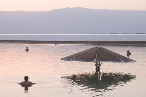 a man sitting in the water with an umbrella at Leonardo Club Hotel Dead Sea - All Inclusive in Ein Bokek