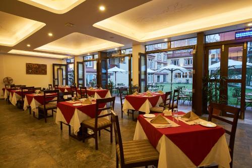 un restaurante con mesas rojas y blancas, sillas y ventanas en Shambaling Boutique Hotel en Katmandú