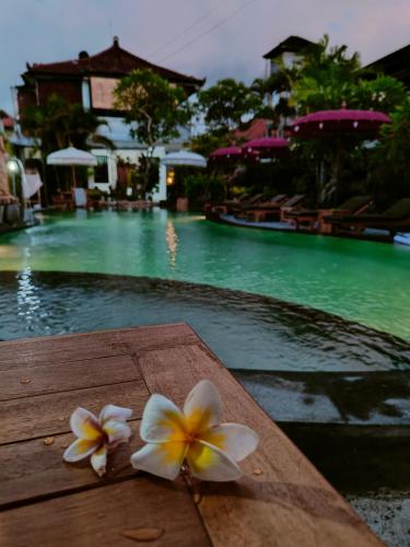 two plumeria flowers sitting on a table next to a pool at Berlian Inn Kuta Beach in Kuta