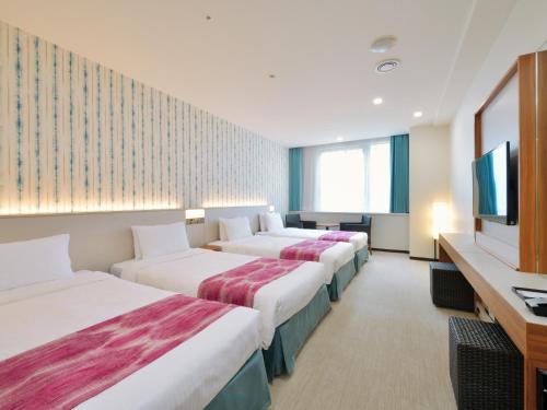 a hotel room with three beds and a flat screen tv at Hotel JAL City Naha in Naha