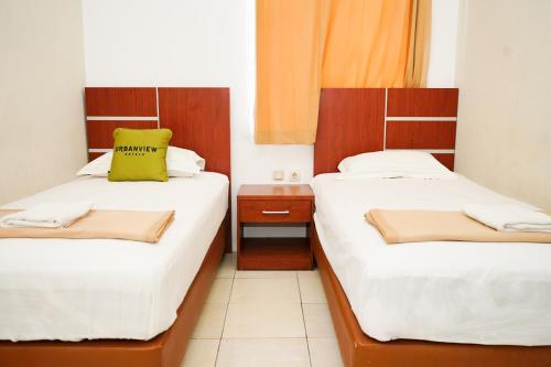 two beds in a small room with a yellow pillow at Urbanview Hotel Ratu Elok Syariah Banjarbaru by RedDoorz in Martapura
