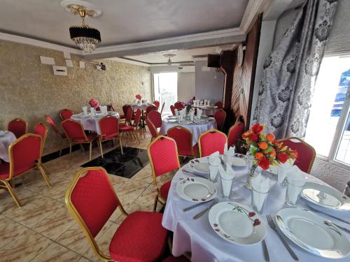 un comedor con mesas blancas y sillas rojas en TCHATCHA HOTEL en Yaundé