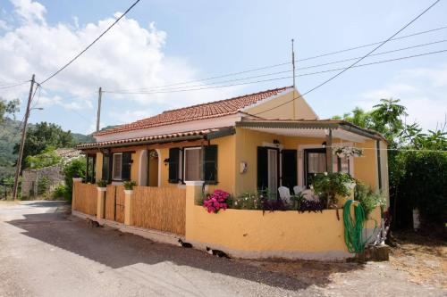 una piccola casa gialla con recinzione e fiori di Zervou House North Corfu a Loútsai