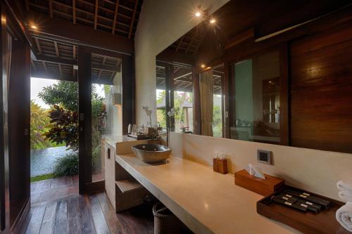 baño con lavabo y espejo grande en Ubud Padi Villas, en Ubud