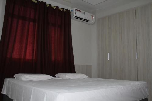 a bedroom with a white bed with a red curtain at Hotel Visconde in Sobral