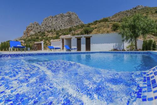a large swimming pool with blue chairs and a building at Alojamiento Rural Caminito del Rey in El Chorro