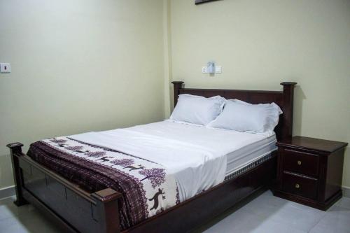 - un lit avec un cadre en bois ainsi que des draps et des oreillers blancs dans l'établissement Fully Furnished 1- Bedroom in East Legon, à Madina