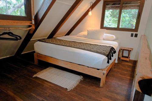 a bed in a small room with two windows at Cabaña Chechen, wooden chalet in tropical garden in Isla Mujeres