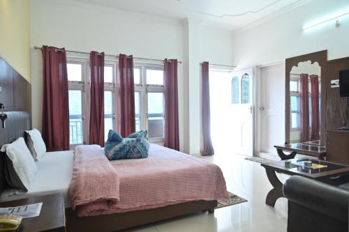 a bedroom with a bed and a desk and windows at Hotel Vasundhara Palace in Chamba