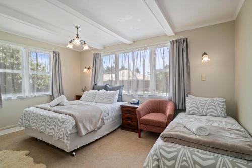 a bedroom with two beds and a chair and windows at Pool House- Springfield in Rotorua
