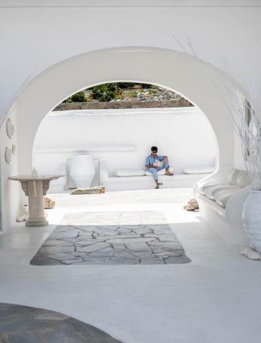 a man sitting on a couch in a white room at Mykonos Bay Resort & Villas in Mýkonos City
