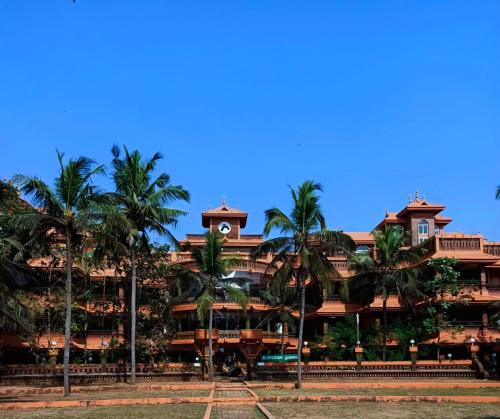 a building with palm trees in front of it at Krishna Beach Resort in Kannur
