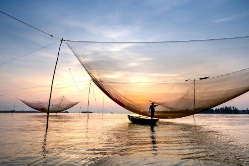 a man on a boat with a large sail in the water at LA GAI HOMESTAY HOI AN in Hoi An
