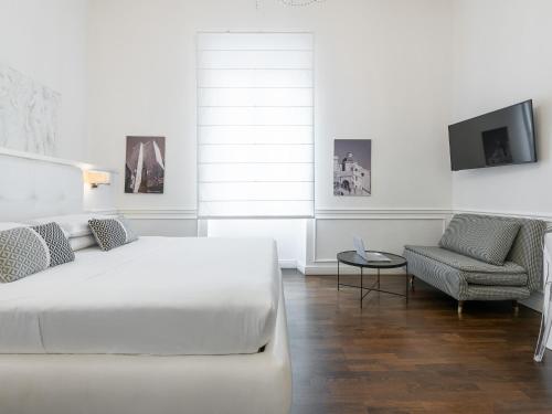 a white bedroom with a bed and a chair at PLEY Cagliari Boutique Rooms in Cagliari