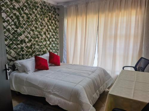a bedroom with a bed with red pillows and a window at Mimosa's @ 44 in Roodepoort