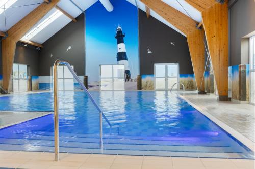 a swimming pool with a lighthouse in the background at Dormio Strand Resort Nieuwvliet-Bad in Nieuwvliet
