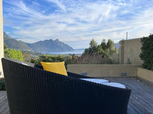 a wicker chair with yellow pillows on a deck with a view at Pure Guest House in Hout Bay