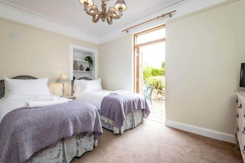 a white bedroom with two beds and a chandelier at Daisybank Kingsbarns - Beautiful 3 Bedroom Cottage in Kingsbarns