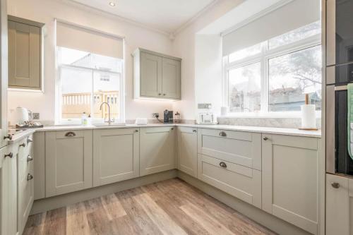 a kitchen with white cabinets and two windows at Daisybank Kingsbarns - Beautiful 3 Bedroom Cottage in Kingsbarns