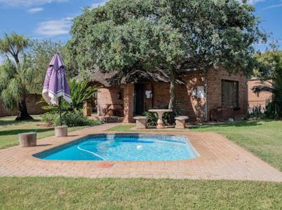 a swimming pool with an umbrella in front of a house at Buffalo Ranch Game Lodge in Groblersdal