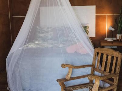 a bed with a mosquito net and a wooden chair at Buffalo Ranch Game Lodge in Groblersdal
