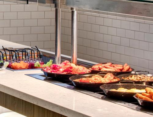 a buffet line with many different types of food in pans at Leonardo London Heathrow Airport in Hillingdon
