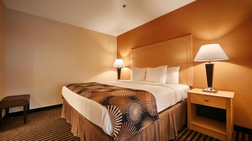 a hotel room with a large bed and a night stand at Best Western Palm Court Inn in Modesto