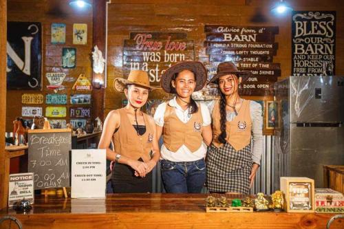 tres personas usando sombreros de vaquero parados detrás de un mostrador en Barn Hostel en Panglao City