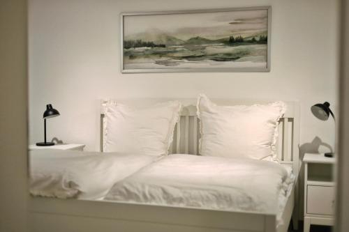 ein weißes Bett mit weißen Kissen und ein Gemälde an der Wand in der Unterkunft Pößnecker Werkstätten - Alte Bäckerei in Pößneck