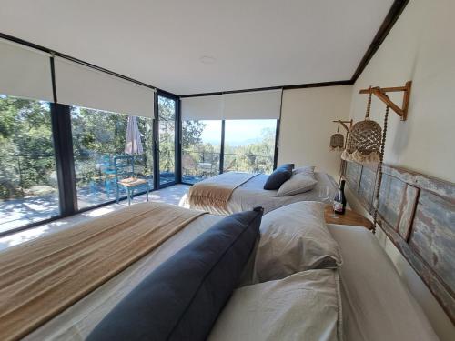 two beds in a room with large windows at Wine Lodge de Viña Vultur en bosque nativo con piscina in Doñihue