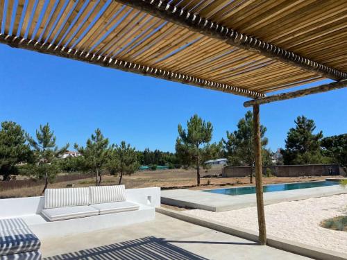 a wooden pergola with a bench and a swimming pool at Casa da Pergola - Beach Design Villa Private Pool in Santo André