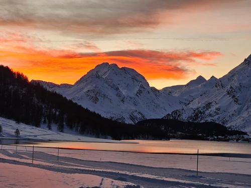 a sunset over a snowy mountain range with a lake at Hotel Ristorante Lagrev in Maloja