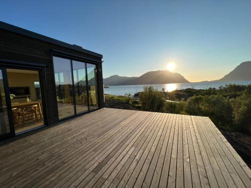 a house with a wooden deck with the sun in the background at Luksushytte sentralt i Lofoten in Kleppstad