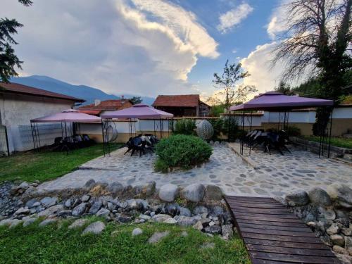 un patio con sombrillas púrpuras, mesas y sillas en Семеен хотел Света Марина en Dobrinishte