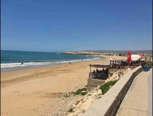 a beach with people sitting on a wall next to the ocean at Superbe appartement pieds dans l’eau in Aourir