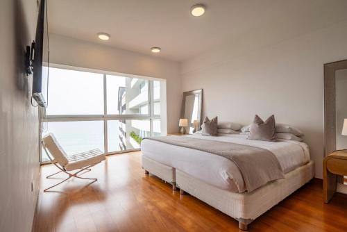 a white bedroom with a bed and a chair at InkaHuset Miraflores Oceanfront in Lima