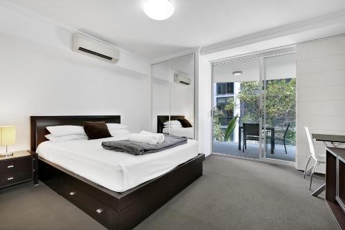 a white bedroom with a bed and a desk and a window at South bank Serviced Apartments in Brisbane