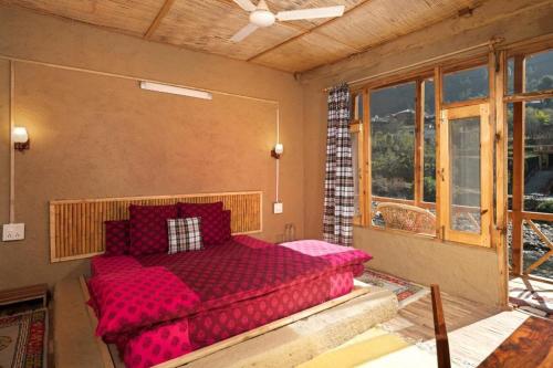 a bedroom with a red bed in a room with windows at Living Good - A Himalayan Boutique Stay in Gushaini