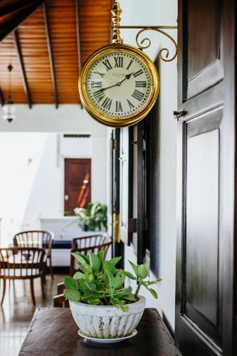 a clock hanging on a wall above a table with a plant at Kaya Residence Kandy in Kandy