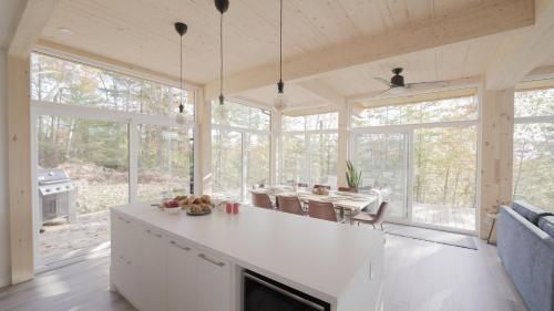 a kitchen with white cabinets and a dining room with windows at Chalet 24 - Modern peaceful retreat near Tremblant in La Conception